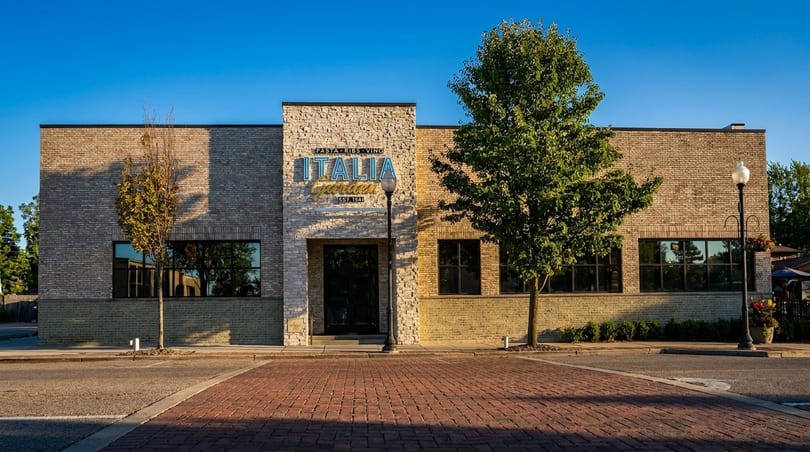 Exterior of Italia Garden restaurant, a brick building with a stone entrance and blue sign, on a sunny day.