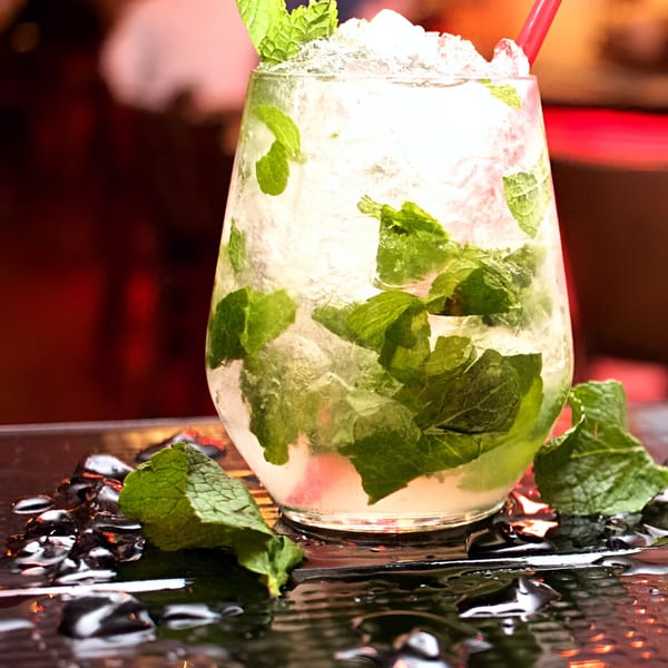 A refreshing mojito cocktail with crushed ice, fresh mint leaves, and a red straw on a wet surface.