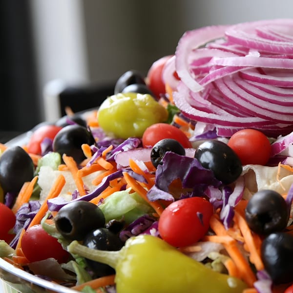 Close-up of a fresh garden salad with lettuce, tomatoes, olives, red onion, and pepperoncini.