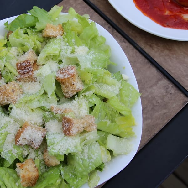 A fresh Caesar salad with croutons and grated cheese, next to a plate of meatballs.