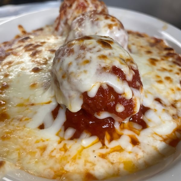 Three meatballs covered in melted mozzarella cheese and marinara sauce in a white bowl.