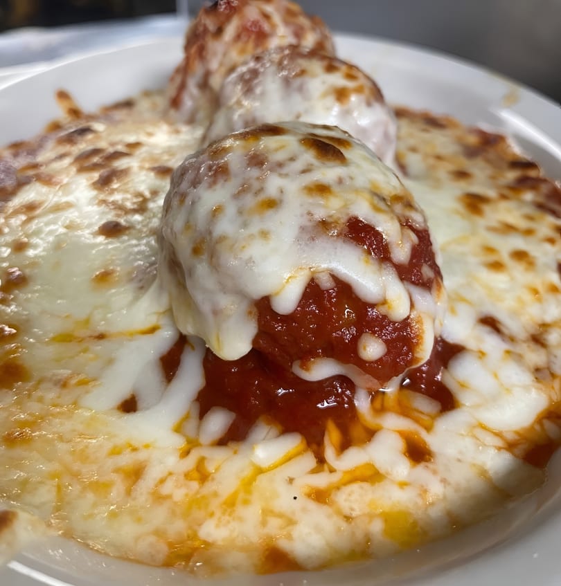 Three meatballs covered in melted mozzarella cheese and marinara sauce in a white bowl.