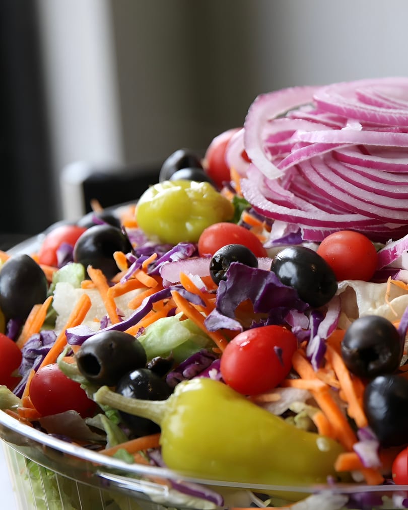 Close-up of a fresh garden salad with lettuce, carrots, red cabbage, olives, tomatoes, and banana peppers.